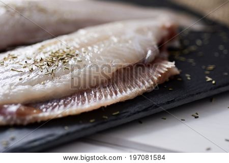 closeup of a pair of raw filleted common sole on a slate tray placed on a rustic wooden table