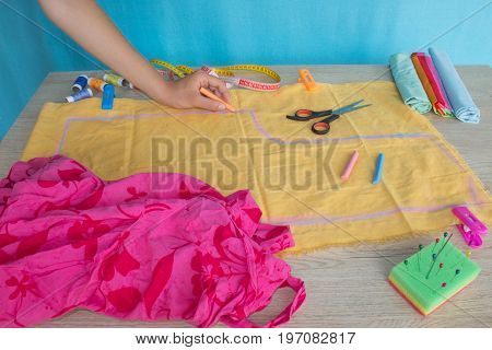 Seamstress hands on the work table with pattern and measuring tape. Tailor hands working with scissor and suit textile cloth