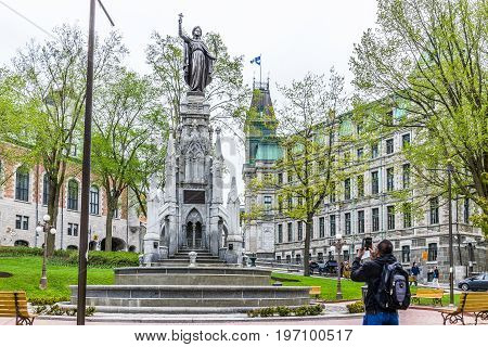 Quebec City Canada - May 29 2017: Tourist man taking picture of fountain called Monument de la Foi by Hotel Chateau Frontenac
