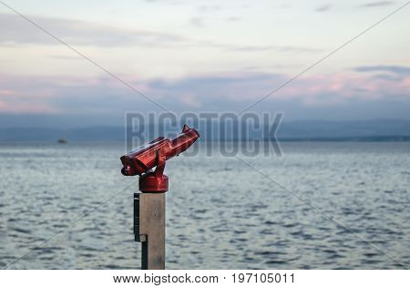 A telescope on the shore of the lake constance in germany in front of blue water and red sky