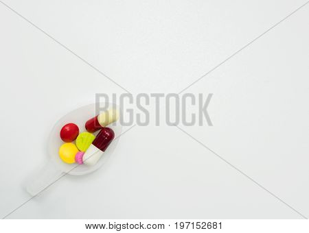 Colorful pills in teaspoon on white background