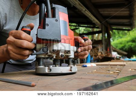 Asian workers using electric routering to cut down stripes on the wood.