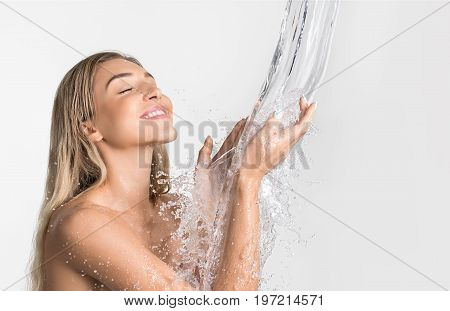 Young beautiful blonde her eyes shut catching water stream and splashes falling in her hands from above studio shot