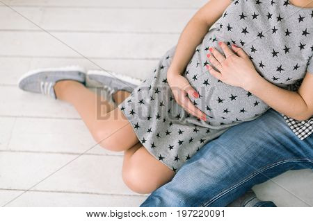 pregnancy family love and happiness concept - closeup on round abdomen of young healthy lady future mother and father sit side by side on white wooden floor expecting child birth happiness.