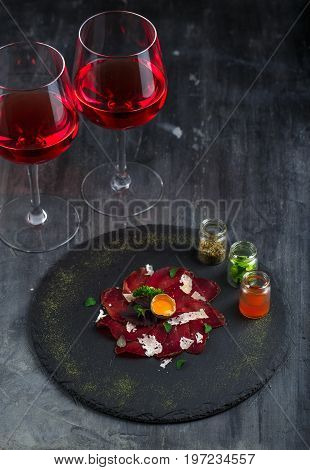 Sliced homemade cured beef with egg and spices on the stone taable, dark photo.