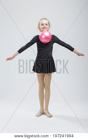 Full Length Portrait of Caucasian Female Rhythmic Gymnast In Professional Competitive Black Suit Posing With Ball in Studio On White. Vertical Image