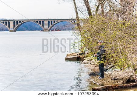 Washington Dc, Usa - March 20, 2017: Person Fishing On Riverfront In Georgetown With Key Bridge In P