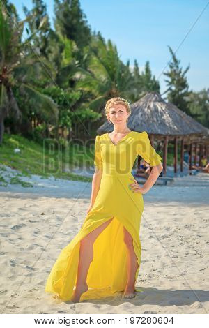 Young woman in yellow dress enjoying vacation on tropical beach. Female posing