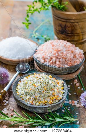 Different types of natural salt in stone bowls on wooden surface. White sea salt pink Himalayan salt Spiced salt with rosemary