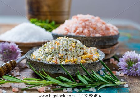Different types of natural salt in stone bowls on wooden surface. White sea salt pink Himalayan salt Spiced salt with rosemary