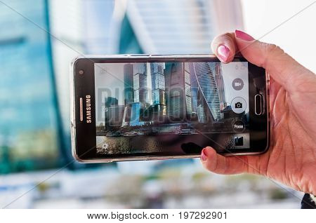 Moscow - May 5 2017: the Samsung cellular phone in woman's right hand. View at the Moscow International Business Cnenter on the screen