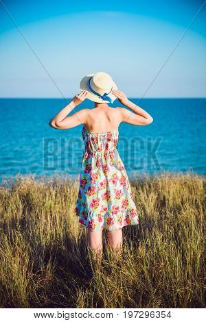 Summer Portrait Of Young Pretty Woman In A Straw Hat And Dress Standing Backwards In The Grass And L