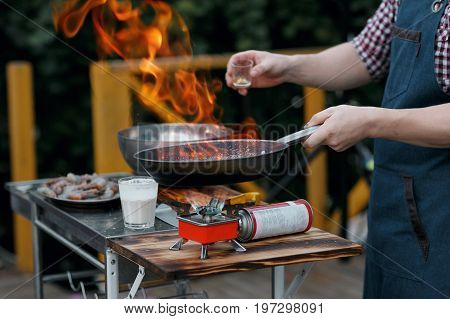 Fried king prawns on iron pan. the chef pours hot sauce. the bake outdoors on a portable gas burner