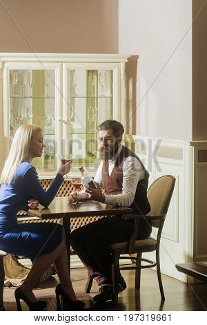 Man and woman dating in restaurant. Hipster and girl with blond hair drinking wine from martini glasses. Couple in love. Alcohol and appetizer. Addictive and convive. Unhealthy lifestyle. Bad habits