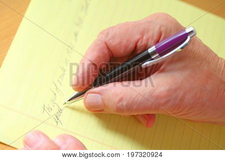 Older man writes in cursive on a ruled yellow pad of paper