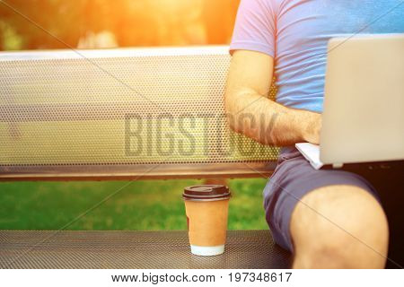 Freelance work.Casual dressed man sitting at wooden beanch inside garden working on computer.. Sun flare