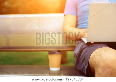 Freelance work. Casual dressed man sitting at wooden beanch inside garden working on computer.. Sun flare