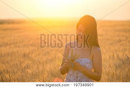 beautiful woman with a wheat bouguet in wheat field at sunset