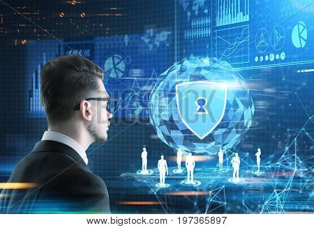 Rear view of a young businessman in glasses looking at a glowing security shield hologram. Blue. Toned image mock up double exposure