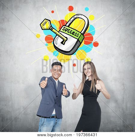 Asian businessman and his blonde colleague wearing an elegant black dress. They are showing thumb up signs and smiling. Concete background key to success sketch.