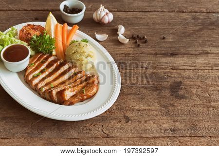 Barbecue pork steak slices on white plate. Delicious pork steak for lunch or dinner on wood table. Moist and soft homemade pork barbecue served with mash potato barbecue sauce and vegetable. Slices pork steak with barbecue sauce on table.