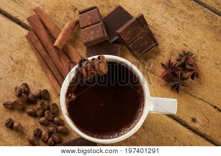 Cup of hot chocolate drink cinnamon sticks boken dark chocolate bar and coffee beans on old wooden rustic table