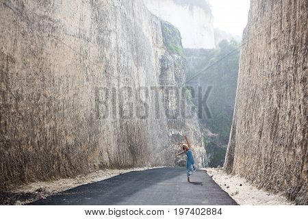 Happy beautiful girl in light-blue dress is going forward on the road between mountains