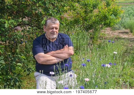 Outdoor portrait of senior Ukrainian peasant sitting in a spring garden and admiring Centaurea flowers