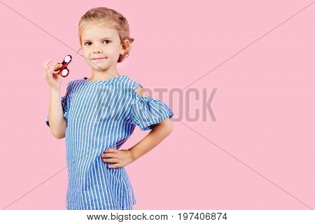 Little beautiful girl in blue stripped shirt is playing red spinner in hand