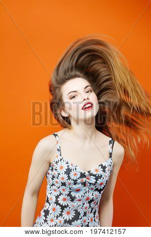 Temperamental Woman With Long Dark Hair Wearing Dress With Flowers Is Having Fun In Studio On Orange