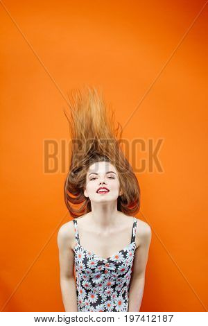 Temperamental Woman With Long Dark Hair Wearing Dress With Flowers Is Having Fun In Studio On Orange