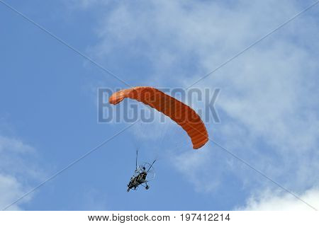 Flight of a motor paraplan with a red wing against a blue sky