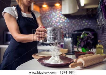 Woman sifting flour through sieve In the kitchen. Selective focus.