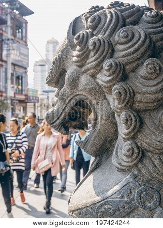Shanghai, China - Nov 6, 2016: A stone lion figurine in traditional Chinese style overlooking Fangbang Middle Road. Pedestrians walk by the statue. Image taken from street level.