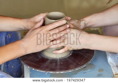 Hands of two people create pot on potter's wheel. Teaching pottery carftman's hands guiding