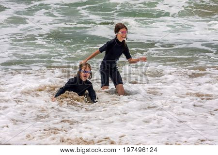 Two girls laughing and playing in the ocean surf. One has fallen down she is laughing so hard.
