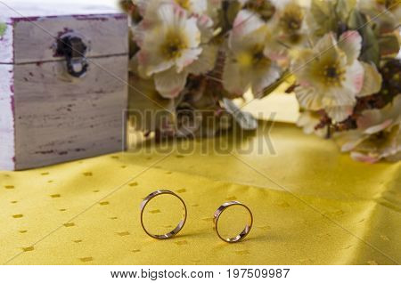 Closeup of wedding rings on the yellow tablecloth background with flowers and old box