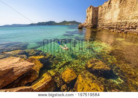 Bikini female looking for fishes in crystal waters by the medieval fortification Methoni Castle, in Methoni, Messenia, Peloponnese, Greece. Summer watersport leisure snorkeling.