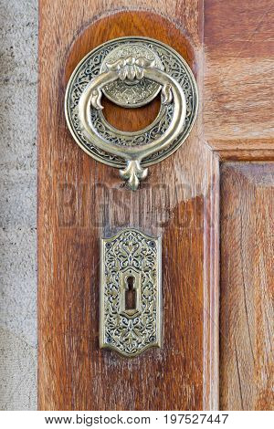 Closeup of antique copper ornate door knocker over an aged wooden door