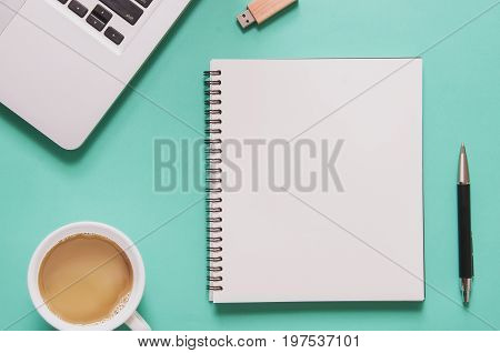 Office workplace concept. Computer laptop with blank notebook cup of coffee pen flash drive on blue background. Top view with copy space flat lay. Pastel color filter.