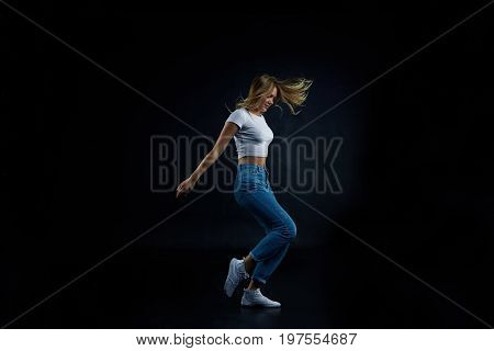 Full lenght studio shot of blonde European girl wearing crop top and blue stretch jeans stretching doing aerobics or dancing. People sports fitness dance energy flexibility and active lifestyle