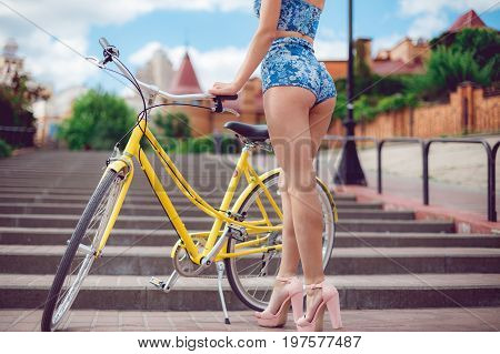 Close up shot of young sexy girl with long nice legs posing with yellow bicycle on city background urban style. Sexy girl in shorts on the bycile.