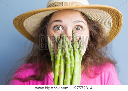 Close-up portrait of funny surprised woman is holding asparagus in front of her face.