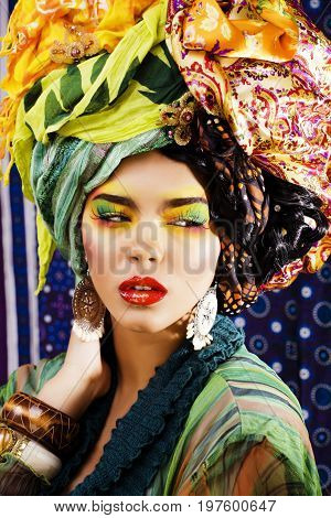 beauty bright woman with creative bright make up, many shawls on head like cubian, ethno look closeup