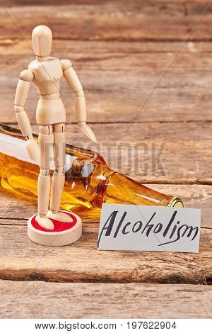 Bottle of alcohol, wooden human dummy. Wooden human puppet, lying bottle, message, wooden background.