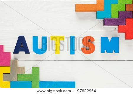 Word Autism built of colorful wooden blocks on a white wooden background with copy space top view. Concept of autism word flat lay. Autism Spectrum Disorder (ASD).