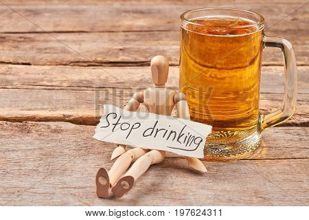 Stop drinking alcohol concept. Human wooden dummy sitting with message near glass of beer.