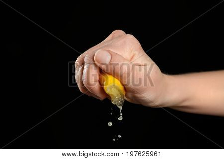 Female hand squeezing half of lemon on black background