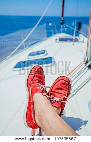 A pair of man legs in red topsiders on white yacht deck. Yachting