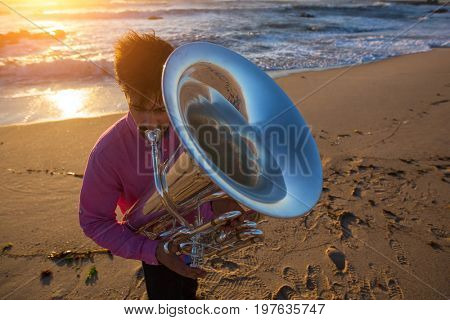 Musician playing the Tuba on the sea coast during an amazing sunset.
